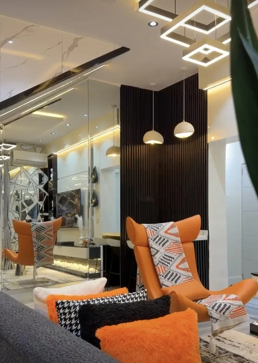 Stylish furnished living room in a Mejee shortlet apartment with orange lounge chairs, feature lighting and a mirrored wall